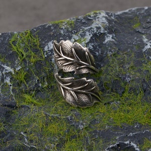 May include: A silver ring featuring a leaf design. The ring is crafted from two leaves that are joined together in the middle. The leaves are detailed and have a realistic appearance.