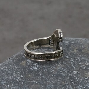 May include: A silver adjustable wrench ring with the words "Sterling Silver 925" engraved on the band.