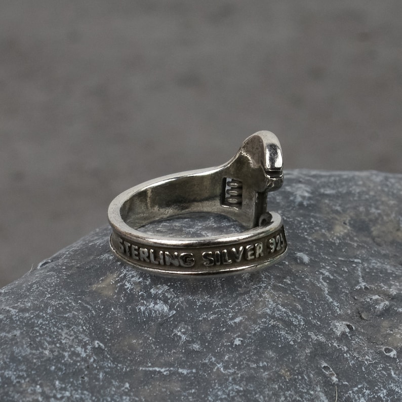 May include: A silver adjustable wrench ring with the words "Sterling Silver 925" engraved on the band.