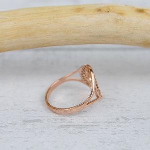 May include: Rose gold ring with an openwork design. The ring features a delicate, symmetrical pattern within a rounded, elongated shape. The band is smooth and polished, and the ring is set against a light, neutral background.
