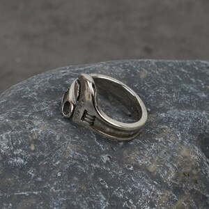 May include: A silver ring shaped like a wrench. The ring has a detailed design and is engraved with the text "1/10 10 K".