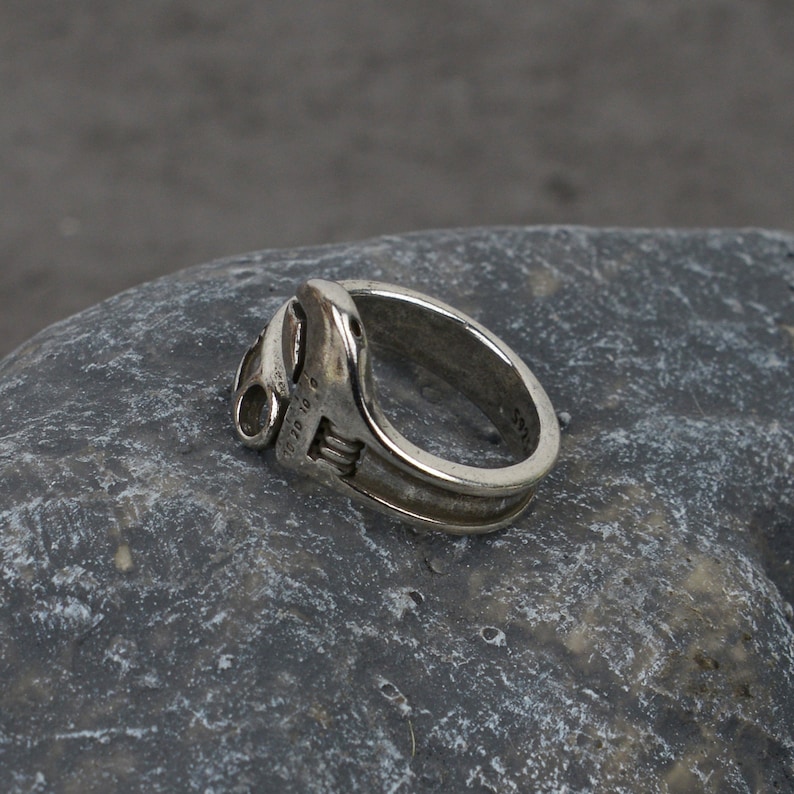 May include: A silver ring shaped like a wrench. The ring has a detailed design and is engraved with the text "1/10 10 K".