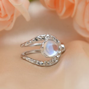 Puede incluir: Un anillo de plata con una piedra de luna engastada en una banda texturizada de forma orgánica.