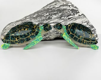 May include: Two green and gold sea turtle figurines facing each other. The turtles have a detailed shell pattern and are made of a smooth, glossy material.