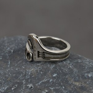 May include: A silver adjustable wrench ring. The ring is made to look like a real wrench with the size markings "10 20 10" on the side.