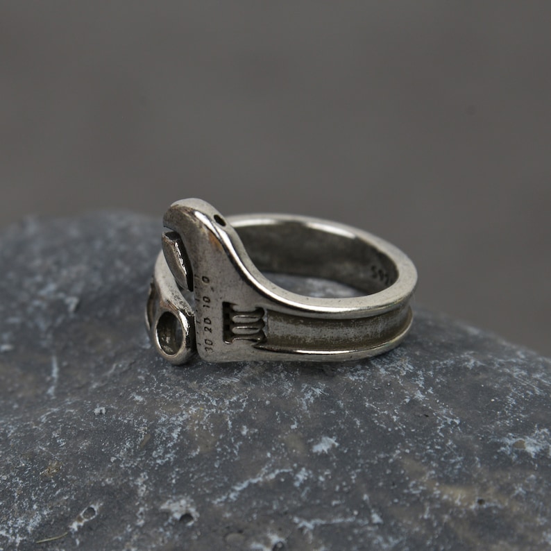 May include: A silver adjustable wrench ring. The ring is made to look like a real wrench with the size markings "10 20 10" on the side.