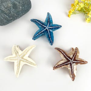May include: Three starfish hair clips in different colors: blue, white, and brown. Each clip has white dots on it.