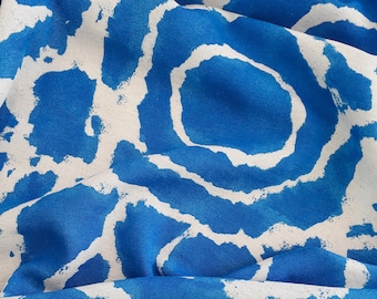 May include: Blue fabric with a white abstract pattern of circles and lines. The fabric is folded and textured.
