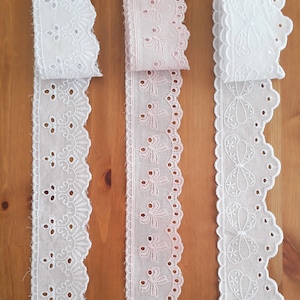 May include: Three decorative lace ribbons in white and pale pink. The white ribbons feature intricate cut-out patterns and scalloped edges. The pink ribbon has a bow design. Ideal for sewing, crafting, and adding a delicate touch to projects.