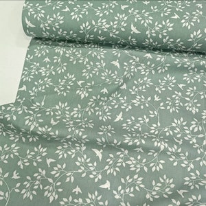 May include: Green fabric with a white pattern of branches and birds. The fabric has a subtle texture.