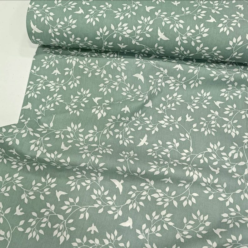 May include: Green fabric with a white pattern of branches and birds. The fabric has a subtle texture.