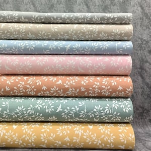 Pode incluir: Uma pilha de oito painéis de tecido com um padrão floral branco sobre um fundo cinza. Os painéis de tecido são de várias cores, incluindo cinza, bege, azul claro, rosa, laranja, verde e amarelo.