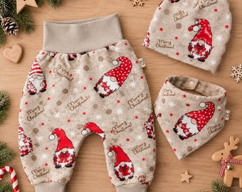 Könnte beinhalten: Ein beiges Baby-Kleidungsset bestehend aus einer Hose mit breitem Bund, einer Mütze und einem dreieckigen Lätzchen. Der Stoff zeigt ein wiederkehrendes Muster aus Weihnachtswichteln mit roten Mützen, roten Sternen und dem Text Merry Christmas.