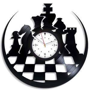 Puede incluir: Un reloj de vinilo negro con una esfera blanca y piezas de ajedrez negras recortadas en el vinilo. Las piezas de ajedrez están dispuestas en un círculo alrededor de la esfera del reloj, y el tablero de ajedrez está recortado en el vinilo debajo de la esfera del reloj.