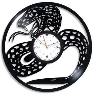 May include: Black vinyl record clock with a snake design. The clock face is white with black numbers and hands.