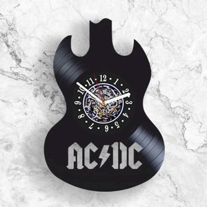 Könnte beinhalten: Schwarze Schallplattenuhr in Form einer Gitarre mit dem Bandnamen "AC/DC" untenaufgedruckt. Das Zifferblatt ist ein weißer Kreis mit schwarzen Zahlen und Zeigern.