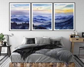 May include: Three framed watercolor paintings of a misty mountain landscape with a blue and purple color scheme. The paintings are hung on a white wall above a gray bed with a black throw blanket.
