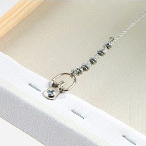 May include: A close-up of the back of a canvas painting with a metal hanging hook and a chain attached to it. The canvas is white and the hook is silver.