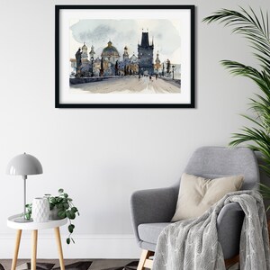 May include: A framed watercolor painting of a bridge with a tower and several buildings in the background. The painting is in shades of gray and blue, with a few touches of green and brown.