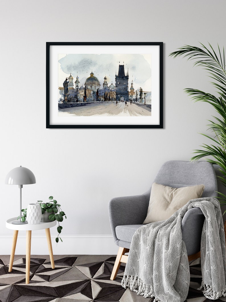 May include: A framed watercolor painting of a bridge with a tower and several buildings in the background. The painting is in shades of gray and blue, with a few touches of green and brown.