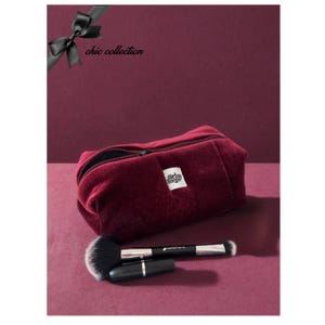 Può includere: Un beauty case in velluto bordeaux con chiusura a zip, un'etichetta bianca con la scritta "girls bags" e un fiocco nero. Un pennello per il trucco e un rossetto nero sono davanti alla borsa. Le parole "chic collection" sono nell'angolo in alto a sinistra.