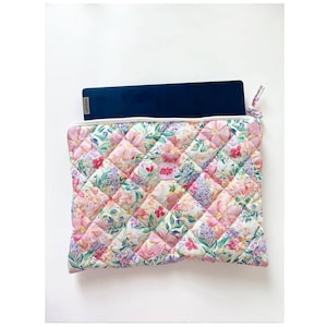 Può includere: Una custodia per laptop trapuntata con un motivo floreale rosa, viola e verde. La custodia è aperta, rivelando un laptop blu scuro con il logo Lenovo. La custodia ha una cerniera bianca e il testo "girlie bags".