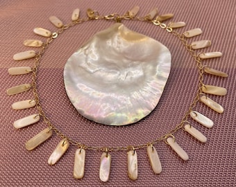 May include: A gold chain necklace with white shell pendant charms. The necklace is displayed on a white shell background.