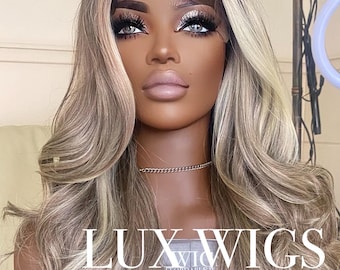 Könnte beinhalten: Eine lange, wellige Perücke mit dunklem Ansatz und blonden Highlights wird auf einem Schaufensterpuppenkopf präsentiert. Die Perücke hat eine Lace-Front und ist mit lockeren Locken gestylt. Der Text "LUX WIGS" ist sichtbar.
