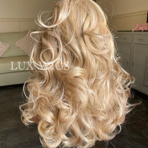 May include: A long, blonde wig with loose curls. The wig is styled in a way that creates volume and movement. The wig is on a mannequin head.