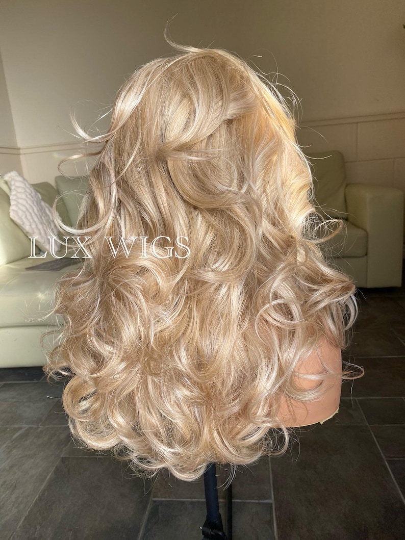 May include: A long, blonde wig with loose curls. The wig is styled with a side part and the curls are cascading down the back.