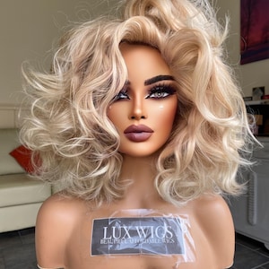 Könnte beinhalten: Eine blonde Perücke mit lockeren Locken, gestylt in einem voluminösen, unordentlichen Look. Die Perücke wird auf einem Mannequin-Kopf präsentiert. Das Etikett auf dem Mannequin lautet "LUX WIGS BEAUTIFUL AFFORDABLE WIGS".