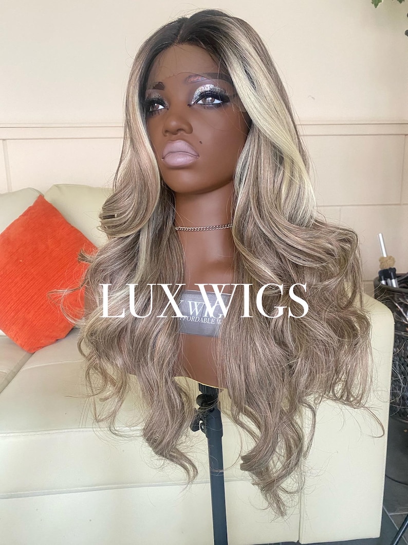 Pu&ograve; includere: Una testa di manichino che mostra una parrucca lunga e ondulata con una miscela di toni marroni, biondi e cenere. La parrucca ha un frontale in pizzo ed &egrave; acconciata con riccioli sciolti. Il testo "LUX WIGS" &egrave; visibile.