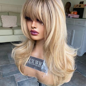 Cathy: jaren 80-kapsel! Korte donkergoudblonde pruik. Blonde pruik met golvend laagje. Blonde pruik. Gelaagde pruik met pony. Donkerder blonde wortel.