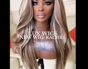 May include: A mannequin head displaying a long, wavy wig with a blend of brown, blonde, and light brown highlights. The wig is styled with a side part and voluminous curls. The text "LUX WIGS NEW WIG: RACHEL" is visible.