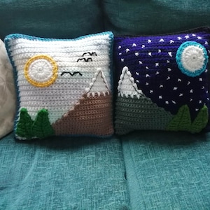 May include: Two crocheted cushion covers with a mountain scene. One cushion cover features a sun and the other features a moon and stars.