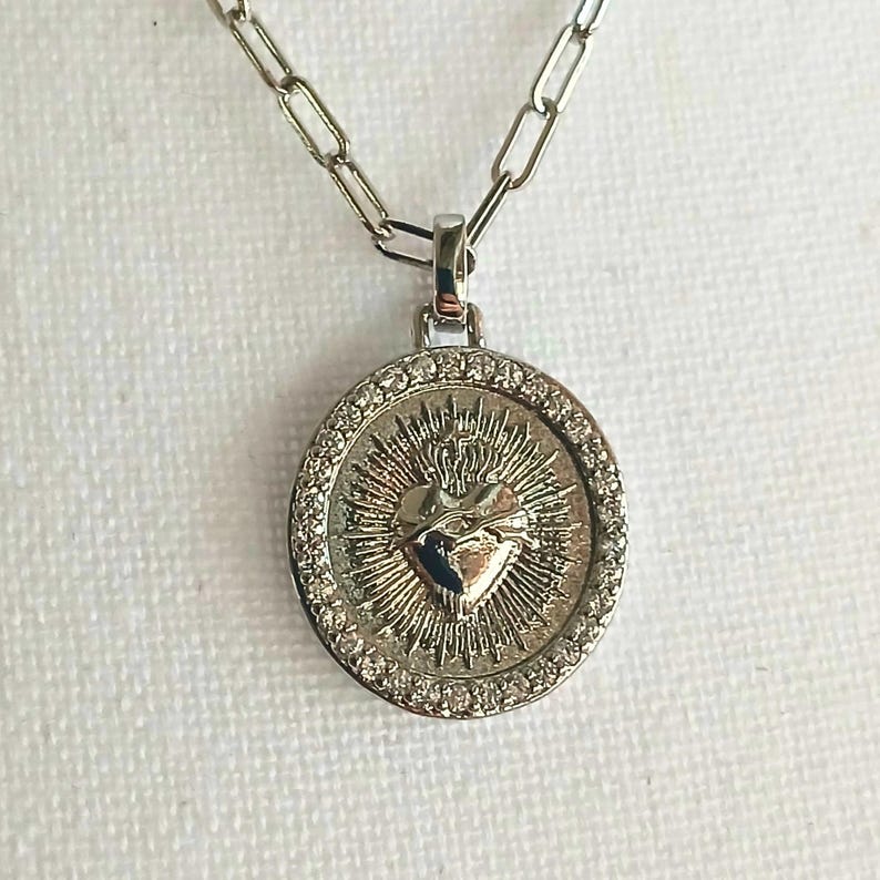 This minimalist necklace features a 18-inch silver-plated chain and a distinctive die-cast metal Sacred Heart Cross pendant. It's a versatile piece, suitable for boys, girls, men, or women. Other chain styles and lengths are available upon request.