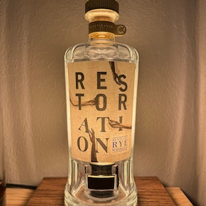 May include: A clear glass bottle with a gold cap and label. The label says "Restoration" and "Kentucky Rye Whiskey".
