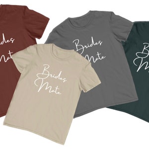 May include: Four t-shirts in different colours with the text "Brides Mate" written in white cursive script.