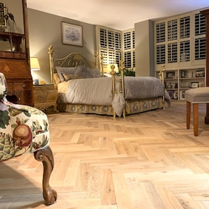 May include: A bedroom with a gold-framed bed, a patterned armchair, and a wooden dresser. The bed has a gray comforter and decorative skirt. The room features light-colored hardwood flooring and a gray upholstered chair with a yellow cushion.