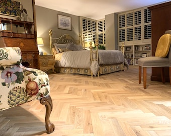 May include: A bedroom with a gold-framed bed, a patterned armchair, and a wooden dresser. The bed has a gray comforter and decorative skirt. The room features light-colored hardwood flooring and a gray upholstered chair with a yellow cushion.