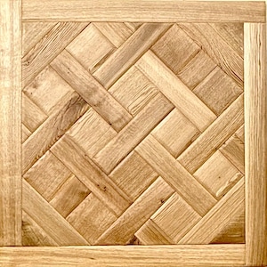 May include: Square wooden panel with a woven pattern. The panel features a light brown color with a natural wood grain texture. The design is framed by a border of the same wood.