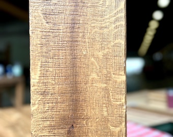 May include: Close-up of a weathered, rectangular wooden beam. The wood grain is visible, with a mix of light and dark brown tones. The texture appears rough and aged, suggesting it may be reclaimed or vintage. The beam is likely part of a larger structure.