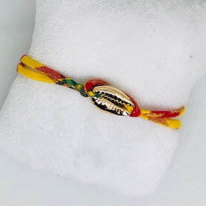 May include: A yellow, red, and green braided bracelet with a gold seashell charm.