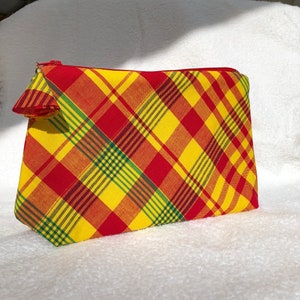 May include: A rectangular, zippered pouch with a vibrant plaid pattern in red, yellow, orange, and green. The zipper is red, and the pouch is made of fabric. The pouch is likely used for cosmetics or other small items.
