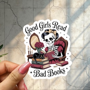May include: A sticker featuring a skeleton reading a book, seated in a maroon armchair. A black cat rests on a stack of books. The text reads "Good Girls Read Bad Books."