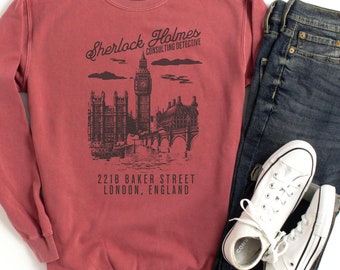 May include: A maroon sweatshirt with a graphic print of the London skyline, including Big Ben, and the text "Sherlock Holmes Consulting Detective 221B Baker Street London, England".