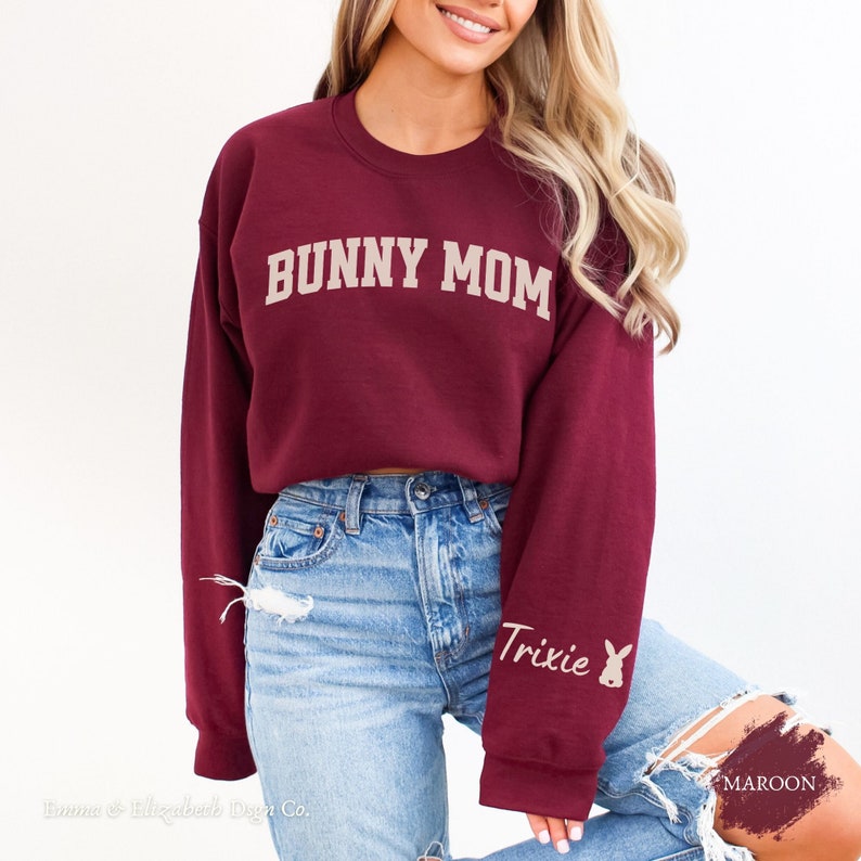 Peut inclure: Sweat-shirt court en bordeaux avec le texte "BUNNY MOM" en lettres cr&egrave;me. La manche gauche porte le texte "Trixie" et une silhouette de lapin en lettres cr&egrave;me.