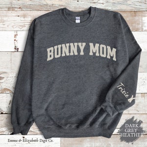 Peut inclure: Sweat-shirt gris fonc&eacute; chin&eacute; avec le texte "Bunny Mom" en blanc sur le devant et le texte "Trixie" avec une silhouette de lapin sur la manche droite.