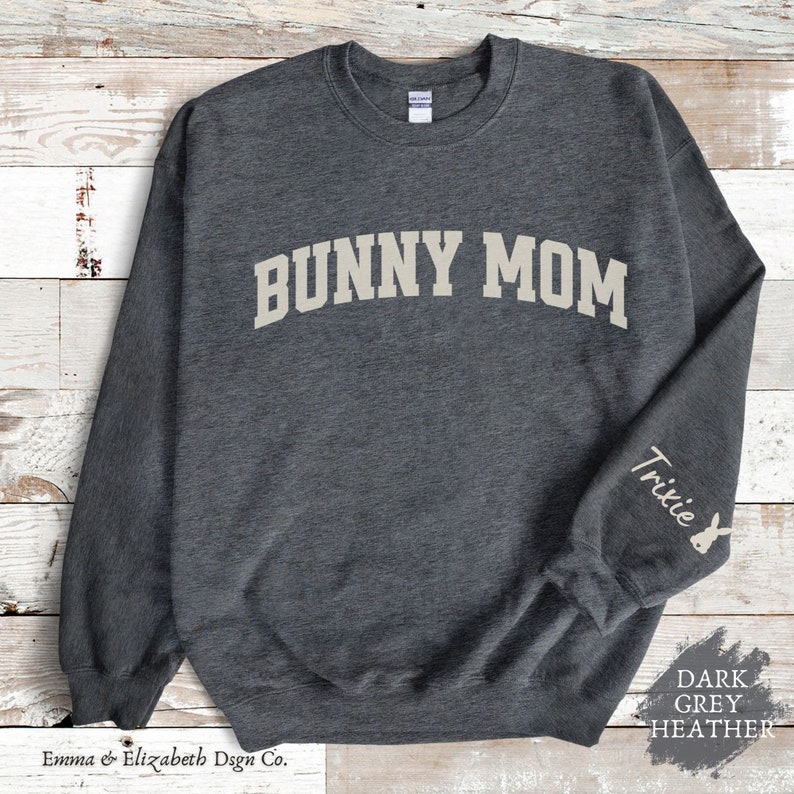 Peut inclure: Sweat-shirt gris fonc&eacute; chin&eacute; avec le texte "Bunny Mom" en blanc sur le devant et le texte "Trixie" avec une silhouette de lapin sur la manche droite.