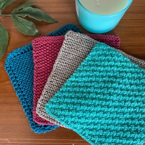 May include: Four knitted dishcloths in different colors: teal, burgundy, gray, and turquoise. The cloths are stacked on top of each other.